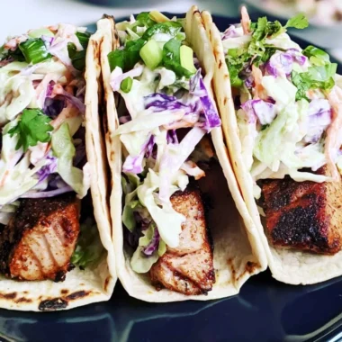 Blackened seared tuna tacos topped with fresh ingredients and lime wedges
