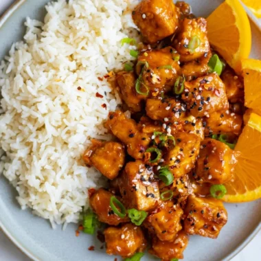 Delicious orange tofu garnished with fresh herbs and served in a bowl.
