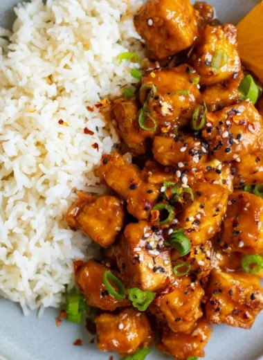 Delicious orange tofu garnished with fresh herbs and served in a bowl.