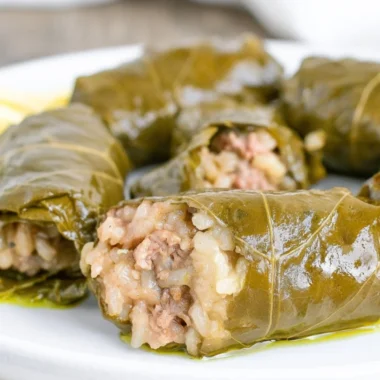 Homemade stuffed grape leaves served on a plate, garnished with lemon slices.