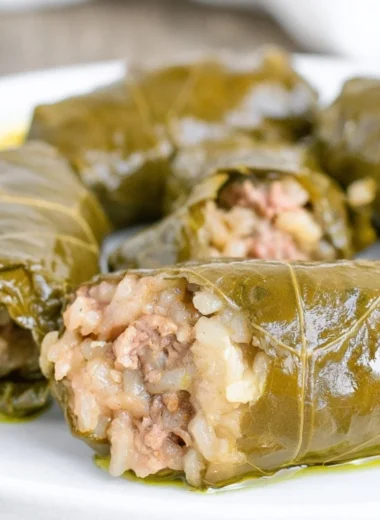 Homemade stuffed grape leaves served on a plate, garnished with lemon slices.