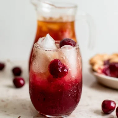 A refreshing glass of cherry pie inspired iced tea with cherries and mint leaves.