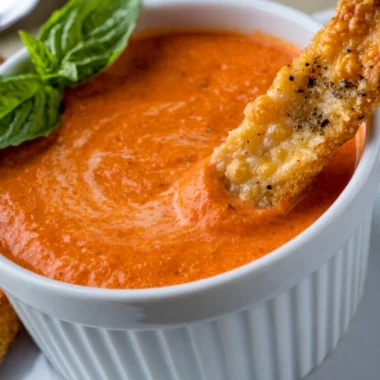 Bowl of creamy tomato soup with Saltine crackers on the side.